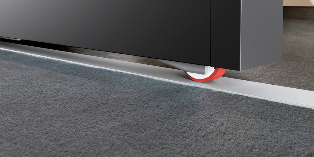 Close-up of sliding door guide wheel moving along recessed floor track beside carpeted floor.