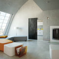 Modern living room with a black door, white walls, and a kitchen in the background.
