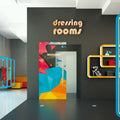 Dressing rooms entrance with colorful door and 'welcome' sign on a gray wall.