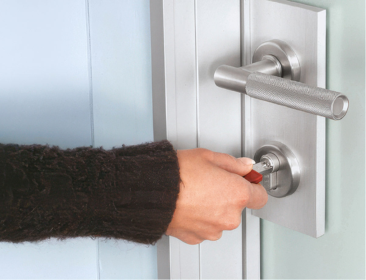 Hand with a key unlocking a metallic door handle.