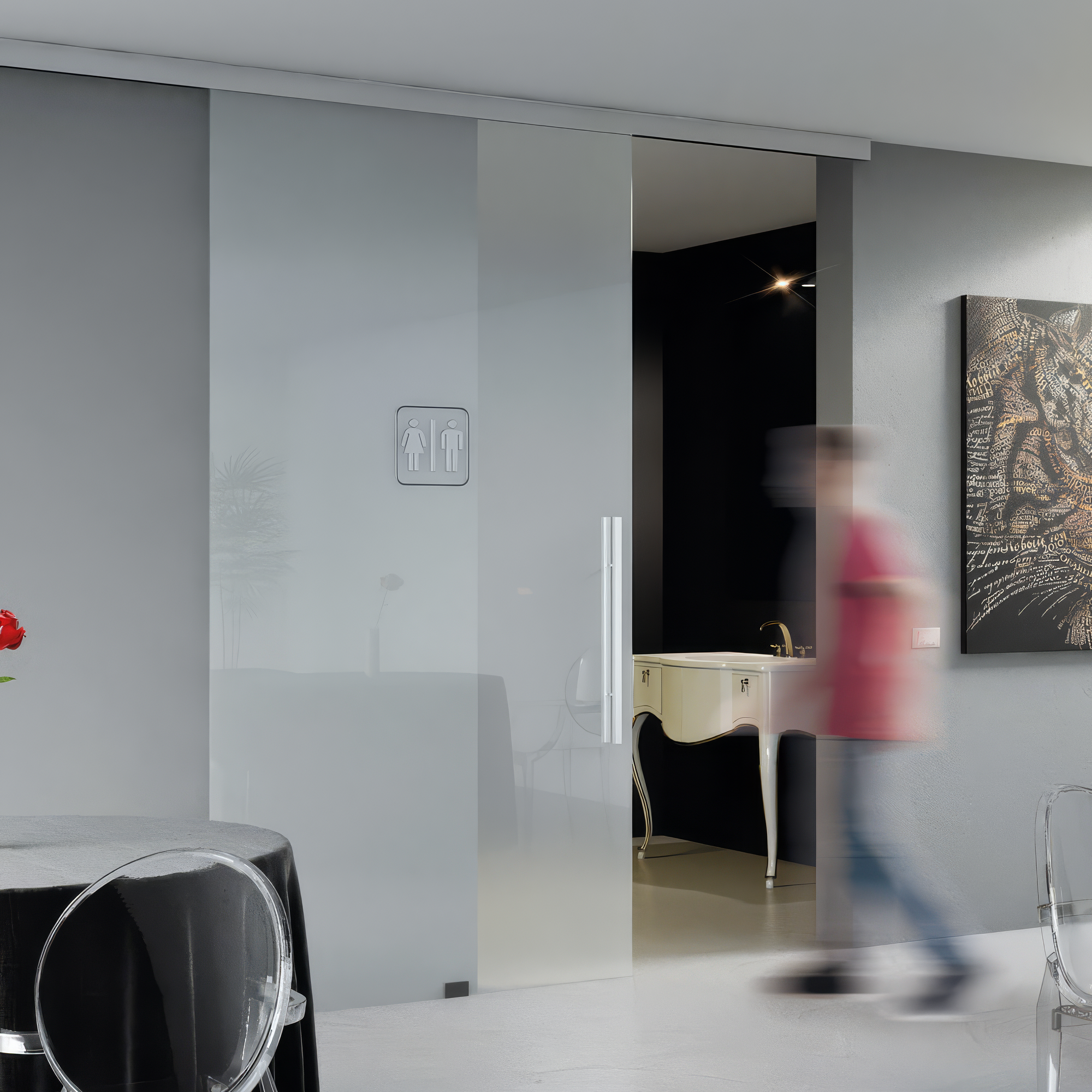 Modern interior with glass sliding door, blurred person, and artwork on wall.